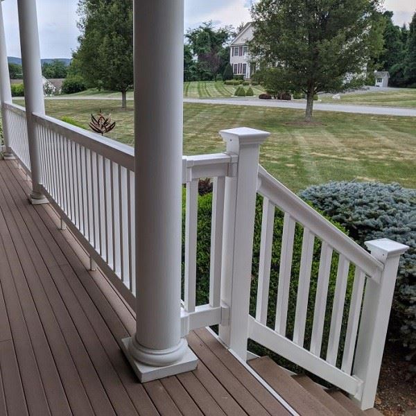 Close-up of a white PVC railing post base connector joining two handrail sections at a stair incline angle, showing the socket engagement and post-to-base mounting hardware Close-up of a white PVC railing post base connector joining two handrail sections at a stair incline angle, showing the socket engagement and post-to-base mounting hardware